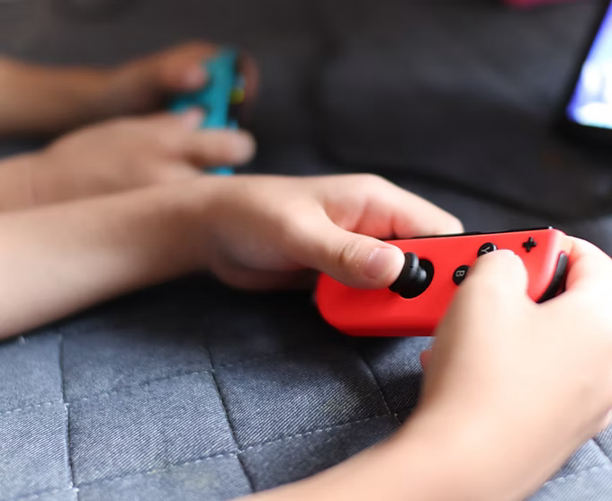 Hands holding red and blue gaming controllers, playing a video game.