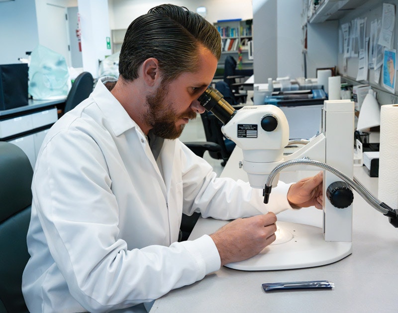 A scientist in a lab coat observes a specimen through a microscope in a laboratory setting.