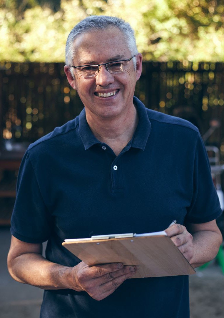 Smiling man holding a clipboard outdoors.