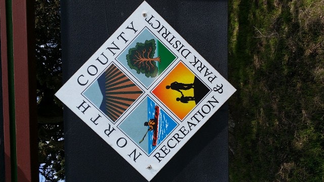 Quadripartite sign with icons representing outdoor activities and nature, labeled "PARK COUNTY RECREATION," rotated 45 degrees, against a nature backdrop.