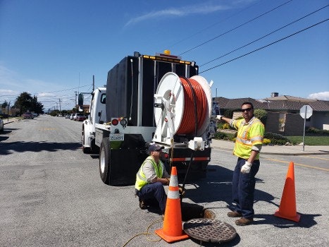 Utility workers with a truck and equipment near a manhole, possibly servicing underground cables or pipes.