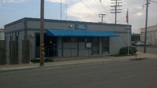 A small building with a blue awning and a sign, situated by a street with utility poles in the background.