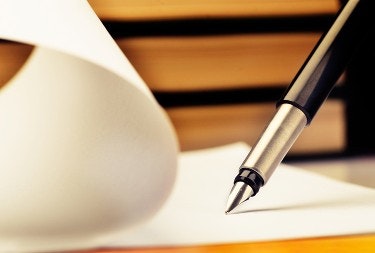 A pen on paper with books in the background.