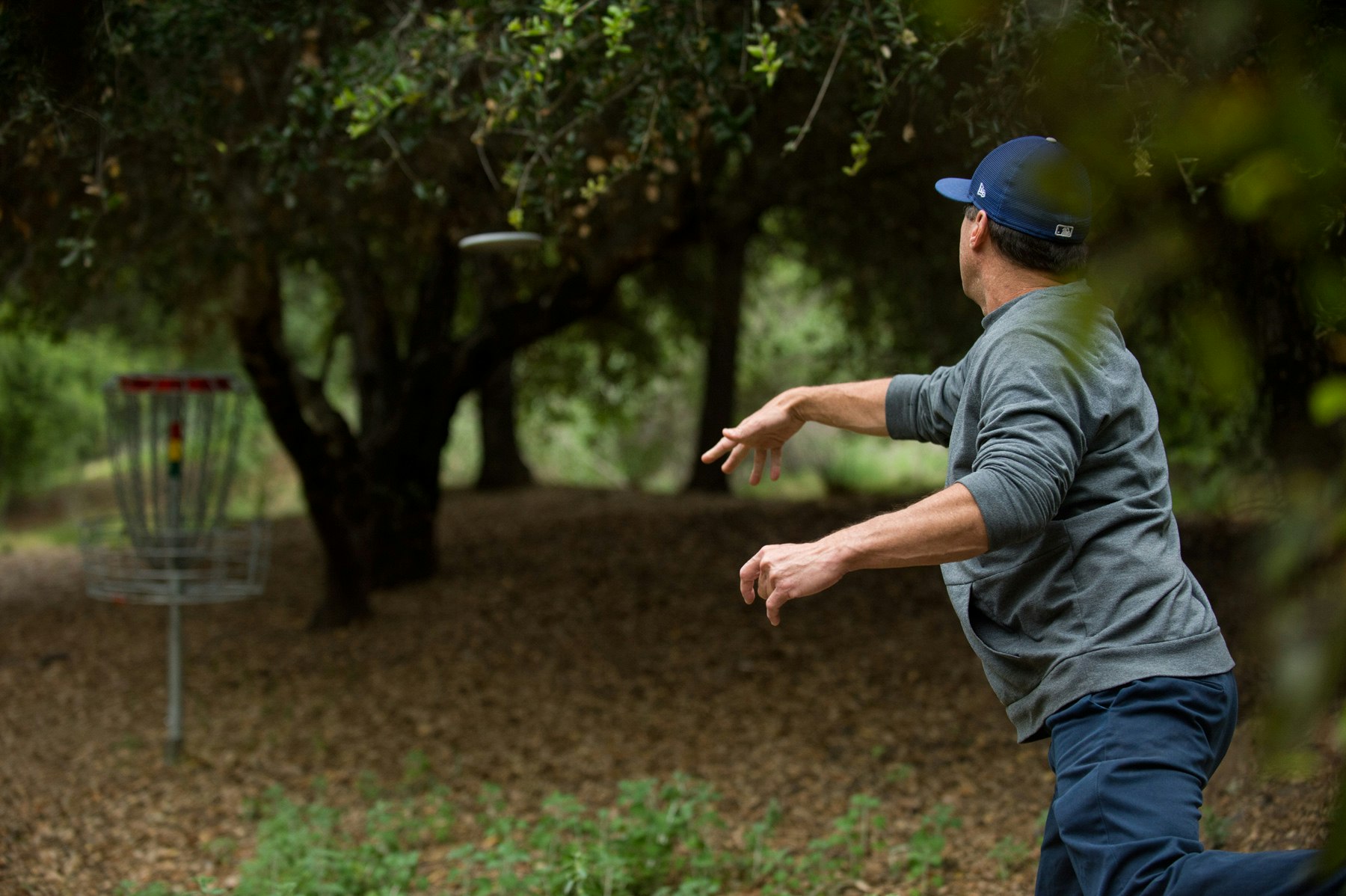 A person throwing a disc towards a disc golf target in a wooded area.