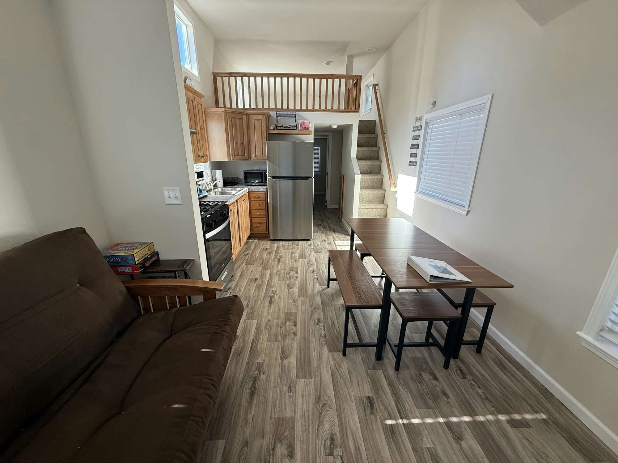 A cozy, bright living space with a kitchen, dining area, and stairs leading to an upper level, featuring a sofa and wood flooring.