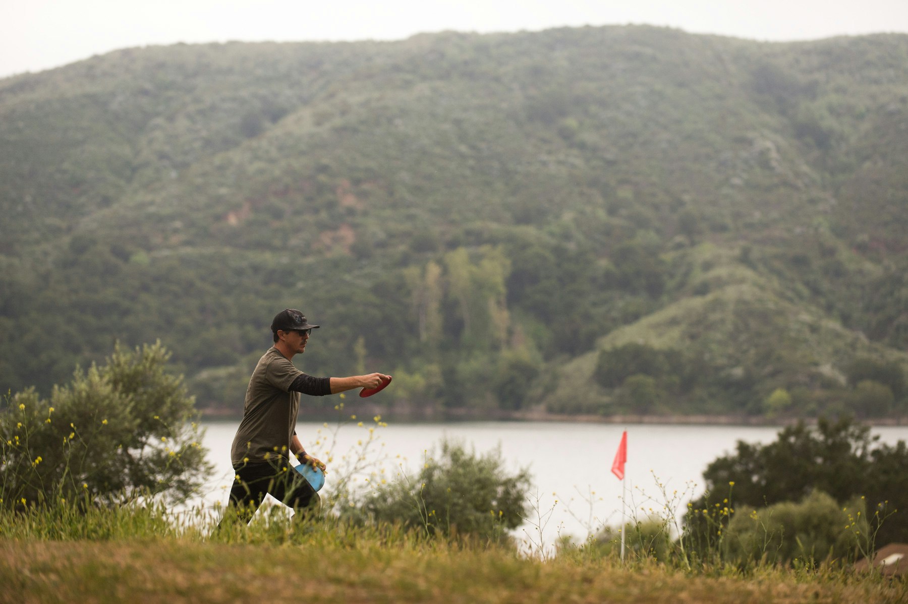 A person playing disc golf, preparing to throw a disc with a lake and mountain in the background.
