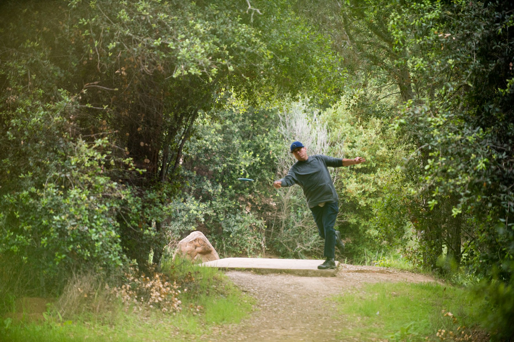 A person throwing a disc in a forested area, likely playing disc golf.