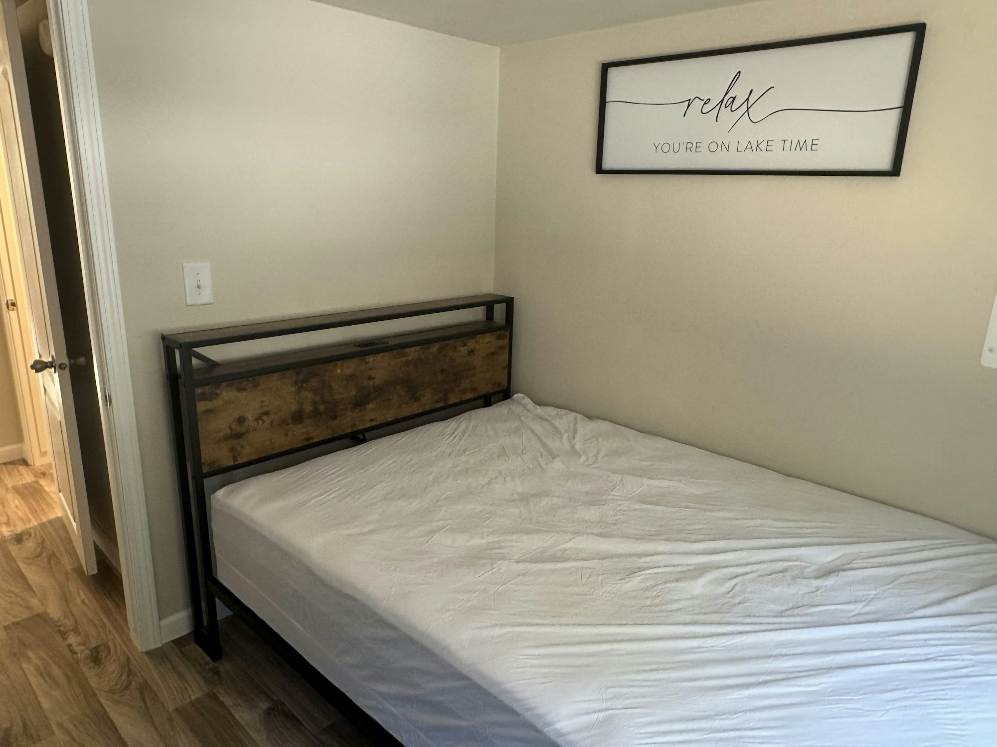 A minimal bedroom with a bed, wooden headboard, and a wall sign saying "relax you're on lake time."