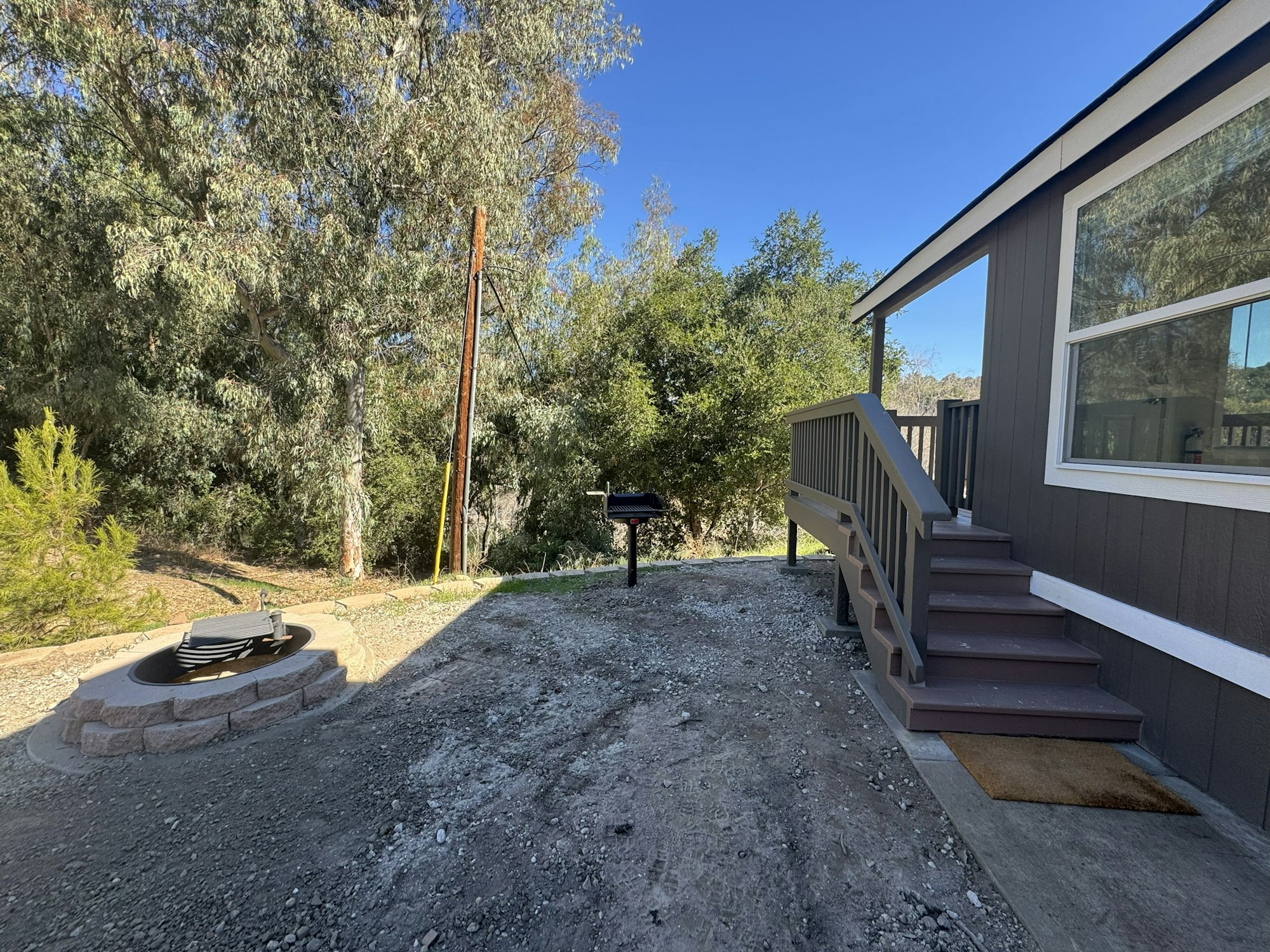 A gravel yard with a fire pit, grill, and side steps leading to a house.