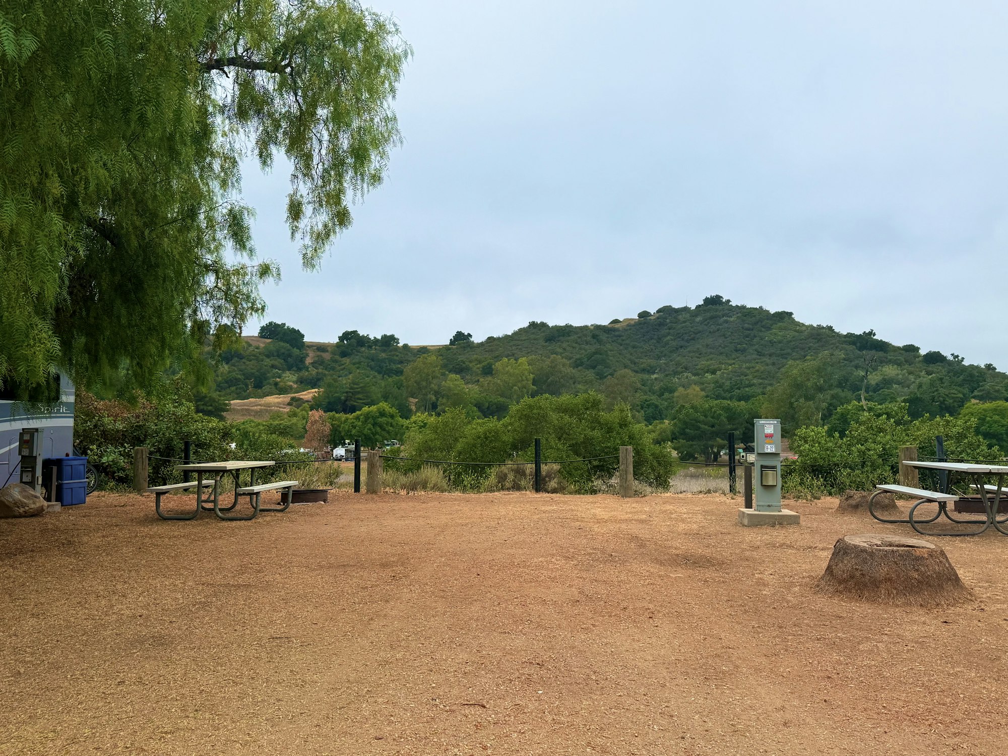 Picnic area with benches in a park, surrounded by trees and hills.