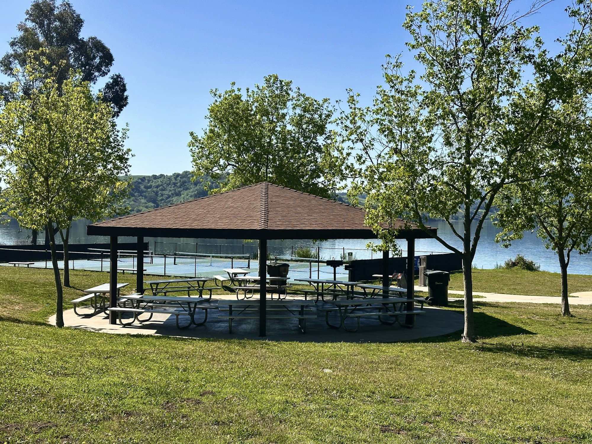 A park with a gazebo, picnic tables, trees, and a lake in the background.