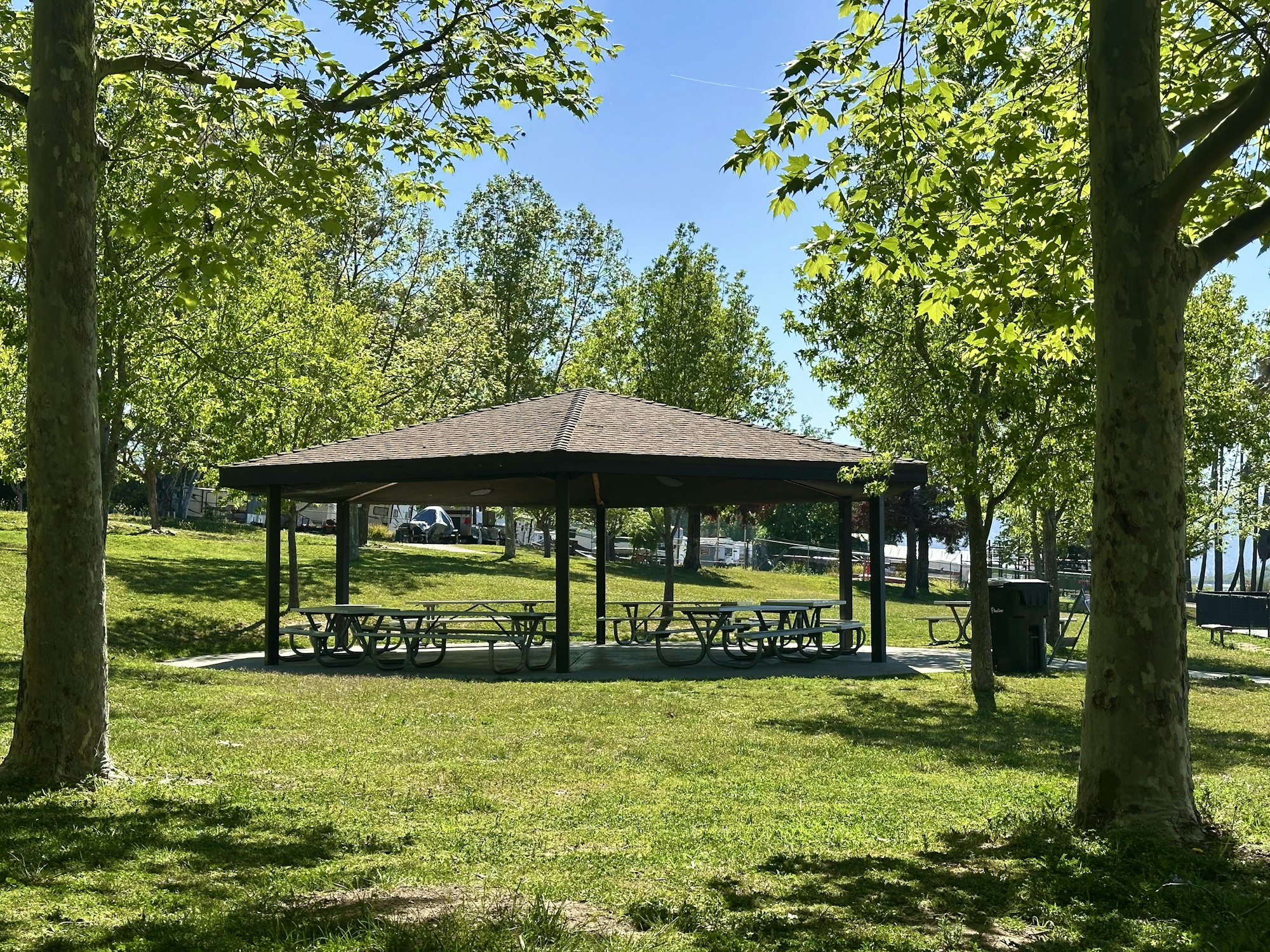 Park with a pavilion, picnic tables, and trash cans surrounded by trees and grassy areas.