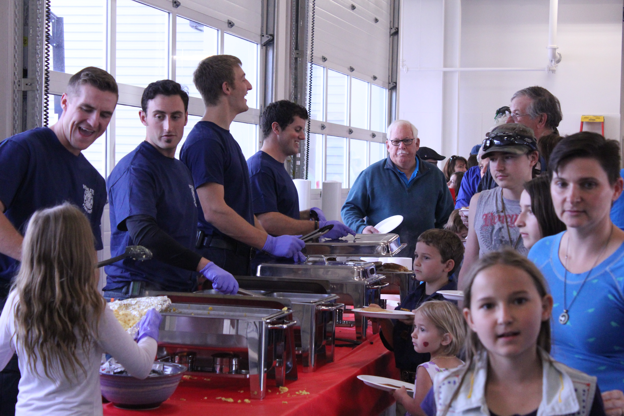 A group serves food at an event, interacting with children and adults in a community atmosphere.