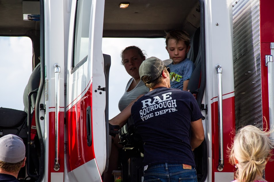 A child interacts with adults near the cabin of a red fire truck, showcasing a community or educational event.
