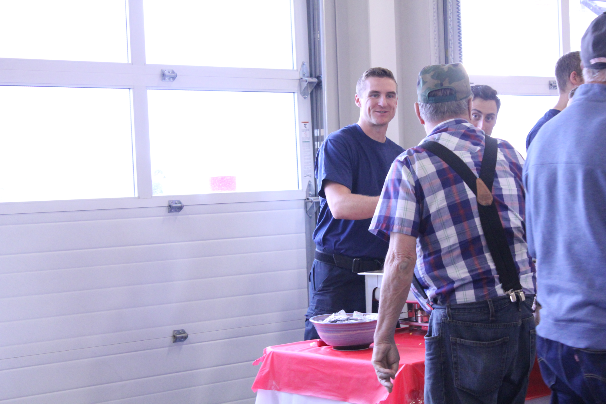 A casual gathering with people chatting, likely enjoying food, in a well-lit space with a red tablecloth.