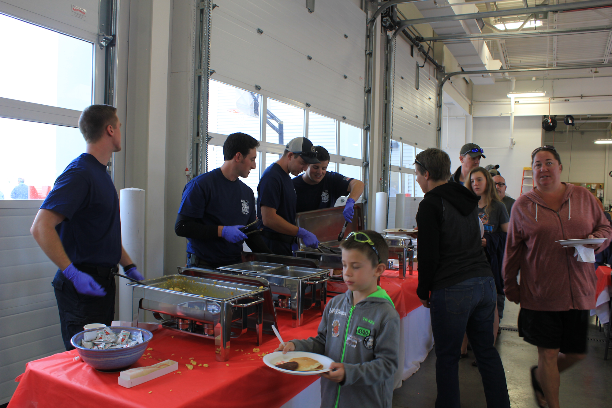A group serves food at a community event, with people enjoying meals and interacting in a gathering space.