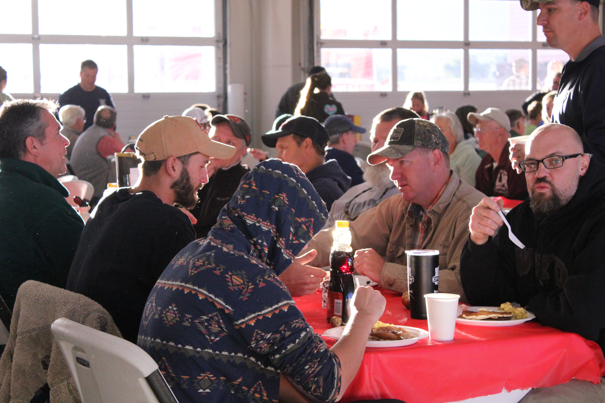 A group of people seated at tables in a dining space, enjoying meals and conversing during a gathering or event.
