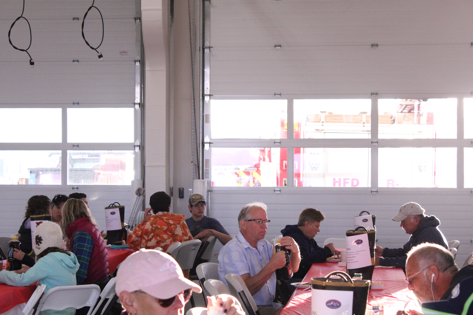 People are seated at tables enjoying a meal in a spacious, brightly lit room, with a visible fire truck outside.