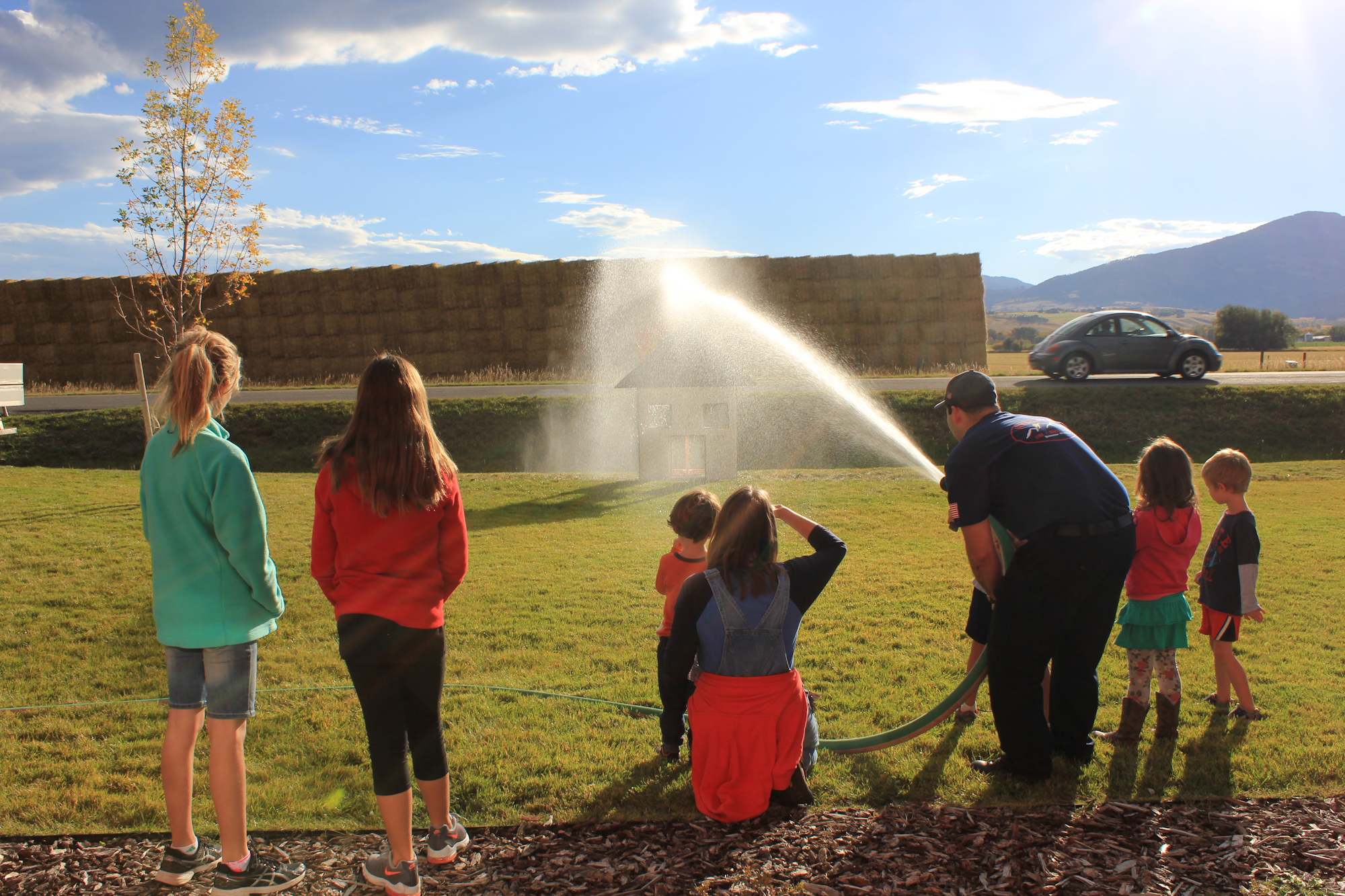 A group of kids watches as a firefighter sprays water from a hose, demonstrating firefighting techniques.