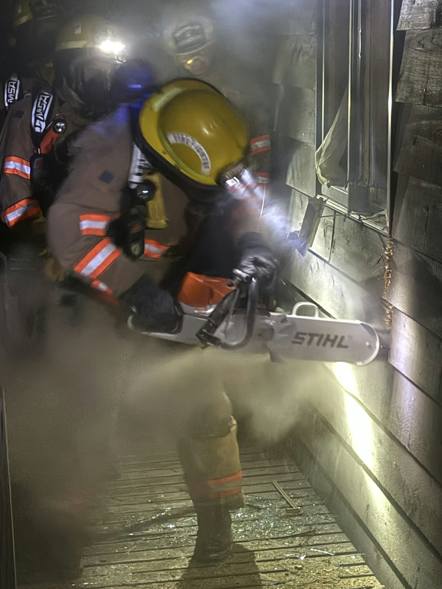 A firefighter using a chainsaw in a smoky environment, possibly during a rescue or training exercise.