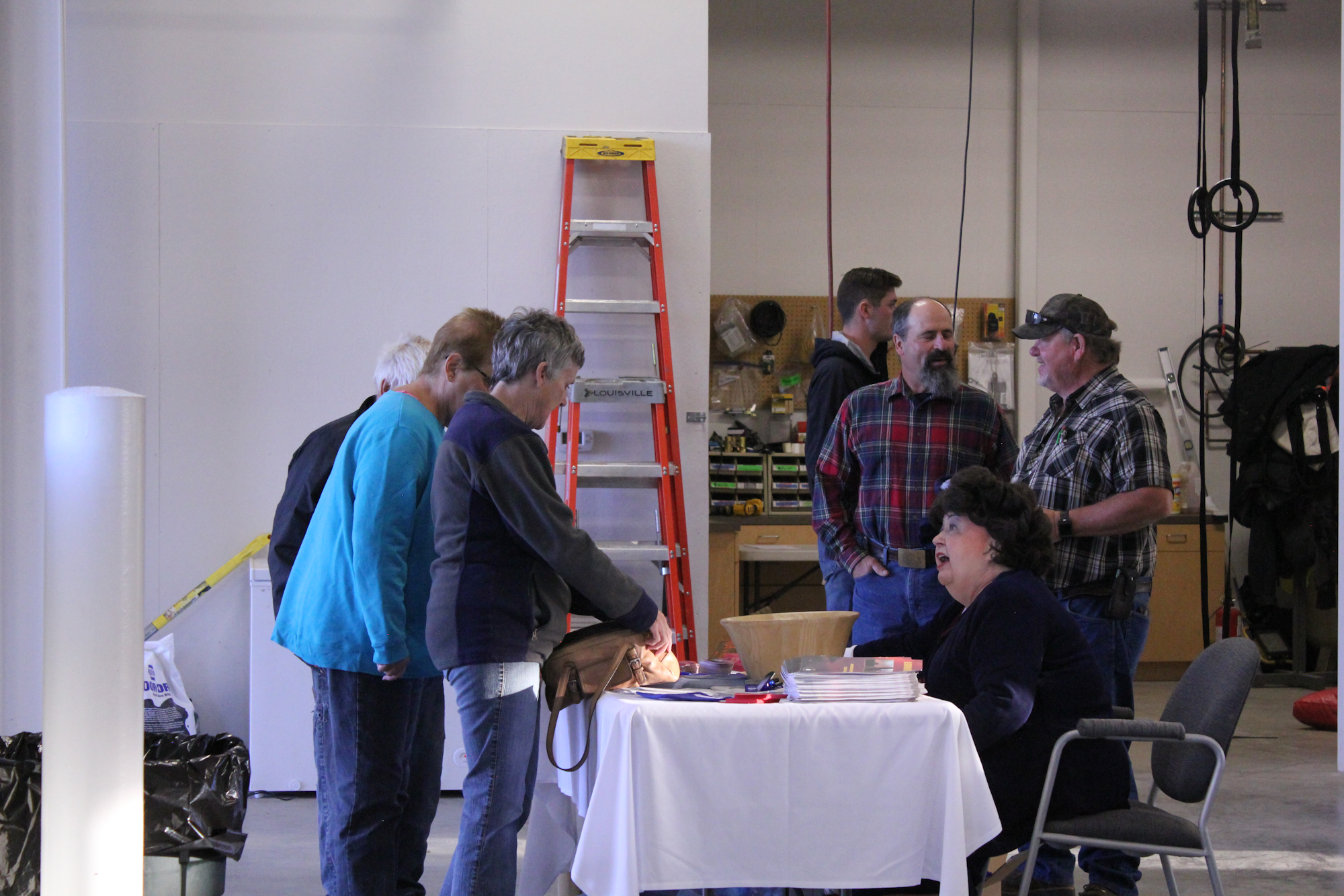 A group of people is gathered around a table in a workshop-like space, engaging in conversation and activities.