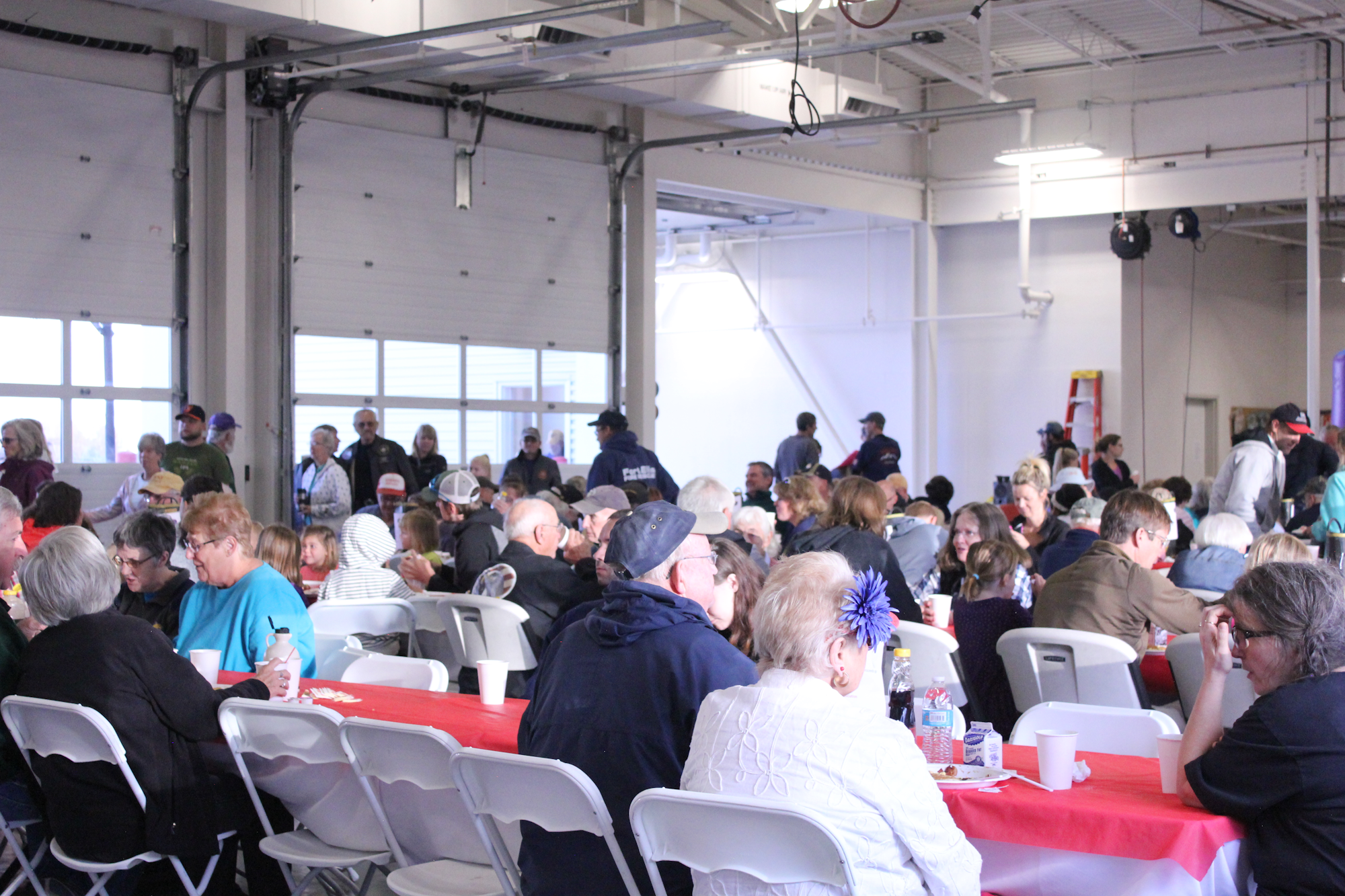 A large gathering of people at tables in a spacious room, likely enjoying food and socializing together.