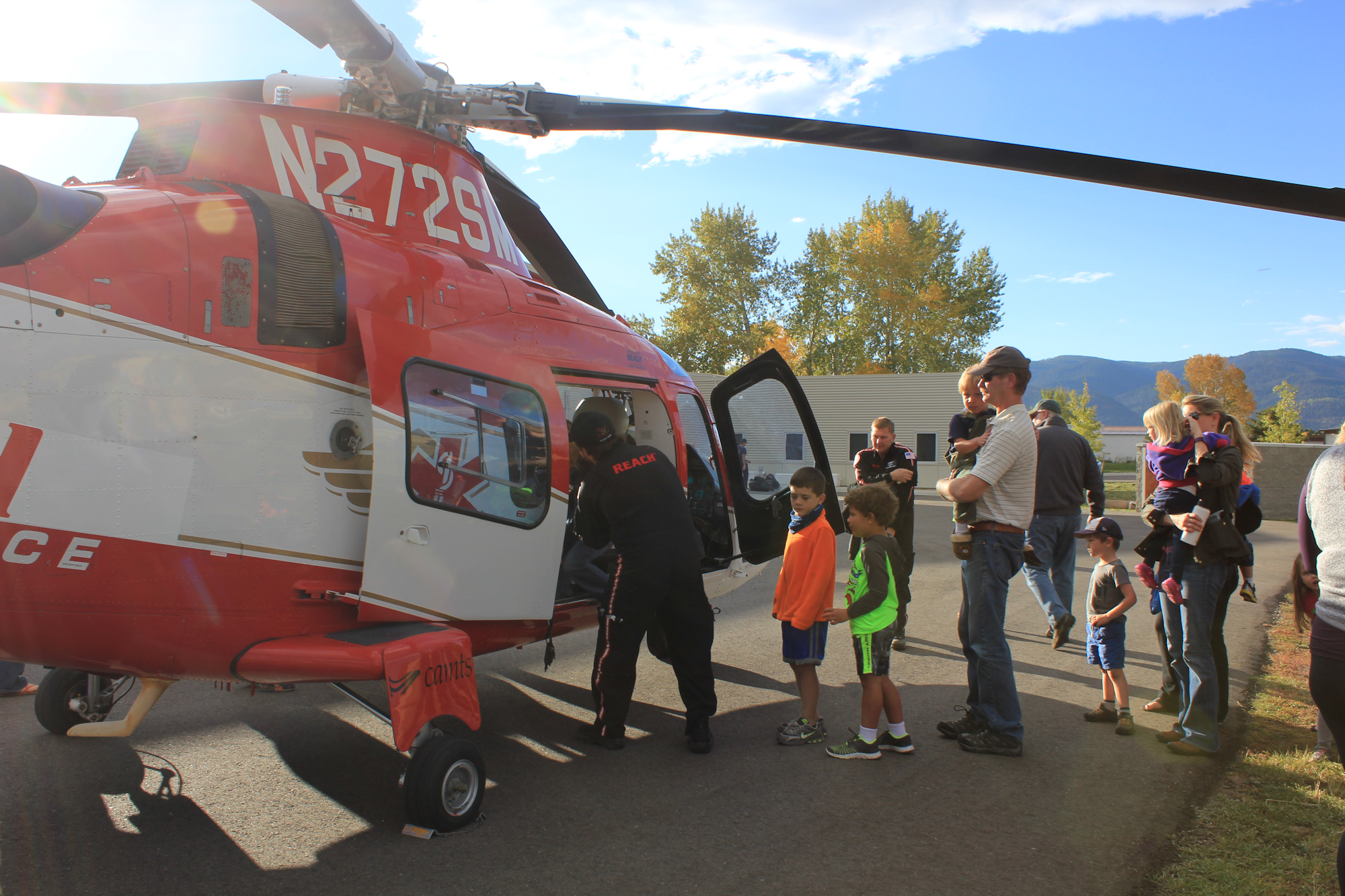 A group of kids and adults gather around a red and white helicopter, with one person boarding it for a demonstration.