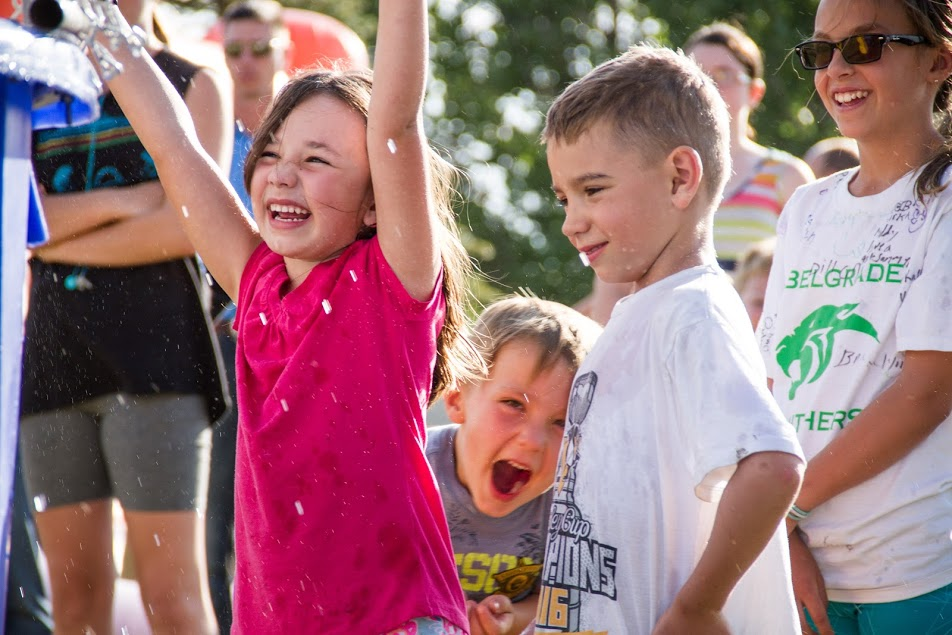 A joyful scene of children playing and celebrating, laughing and enjoying a water event outdoors on a sunny day.
