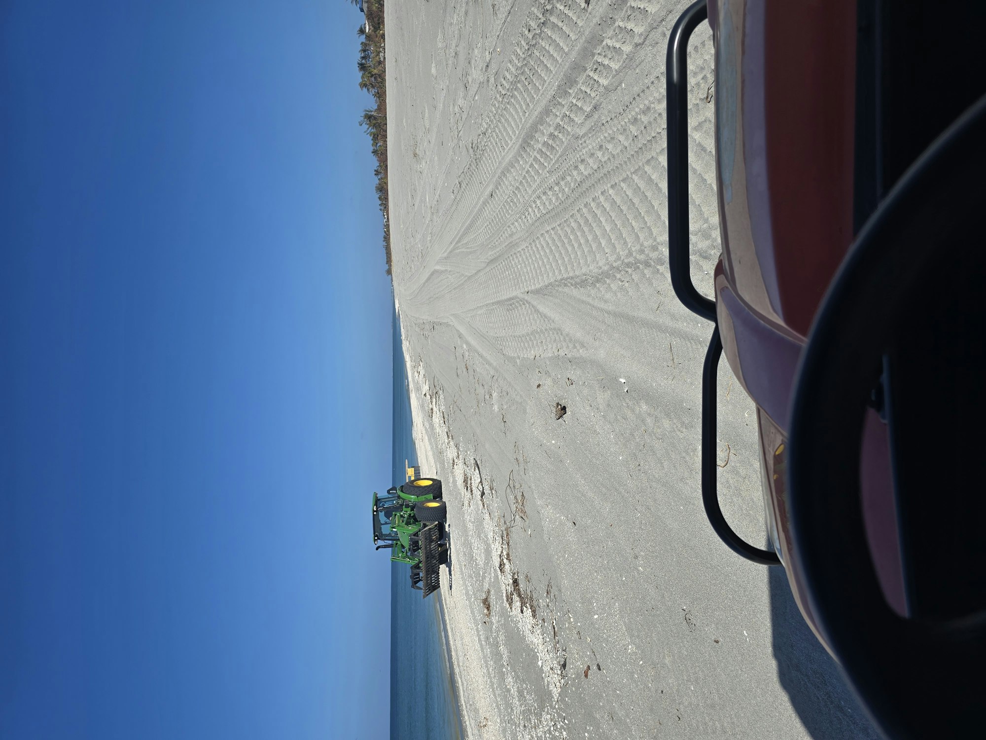 A tractor on a sandy beach with clear blue sky and ocean in the background.