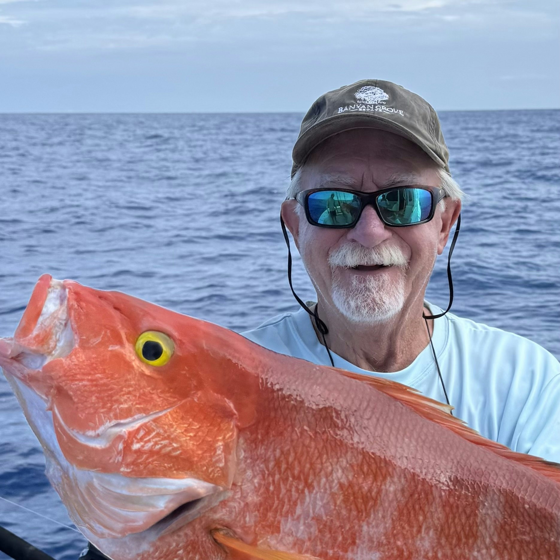 Man holding a large orange fish on a boat, with the ocean in the background.