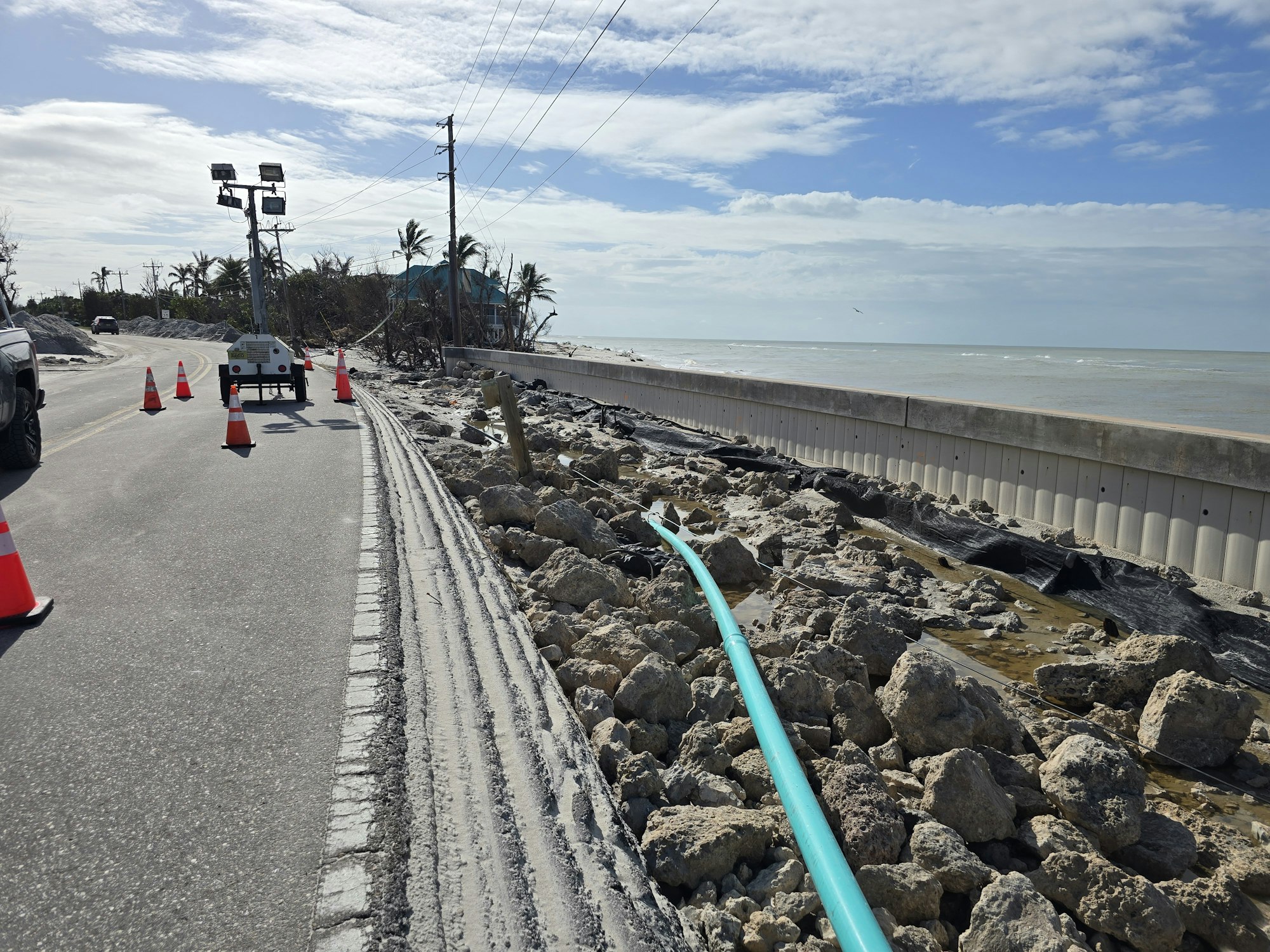 Coastal road construction, traffic cones, temporary lighting, rocks, and ocean view.