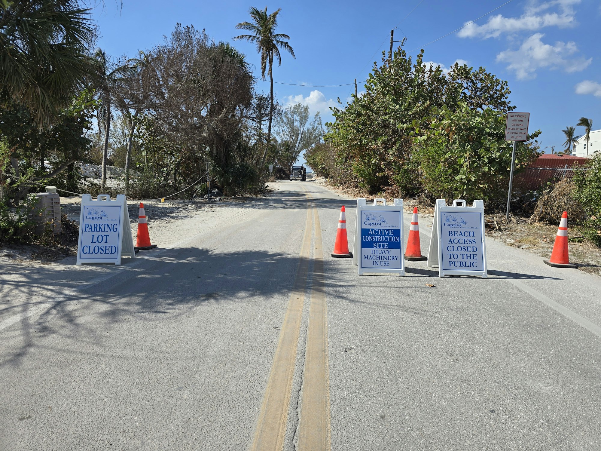 Road with signs: "Parking Lot Closed," "Active Construction Site," "Beach Access Closed to the Public." Orange cones block the path.