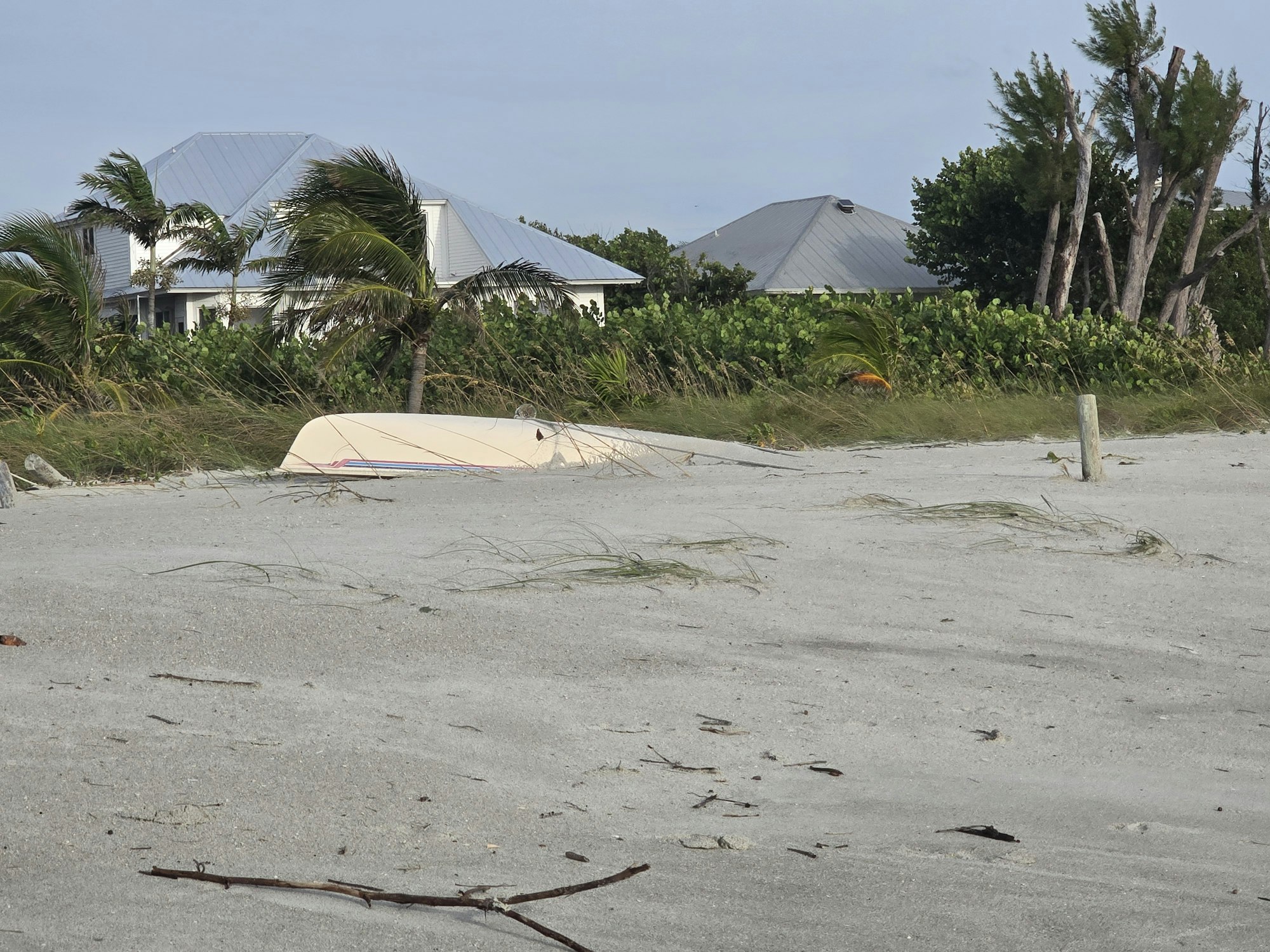 Beach scene with an overturned boat, palm trees, and houses in the background.