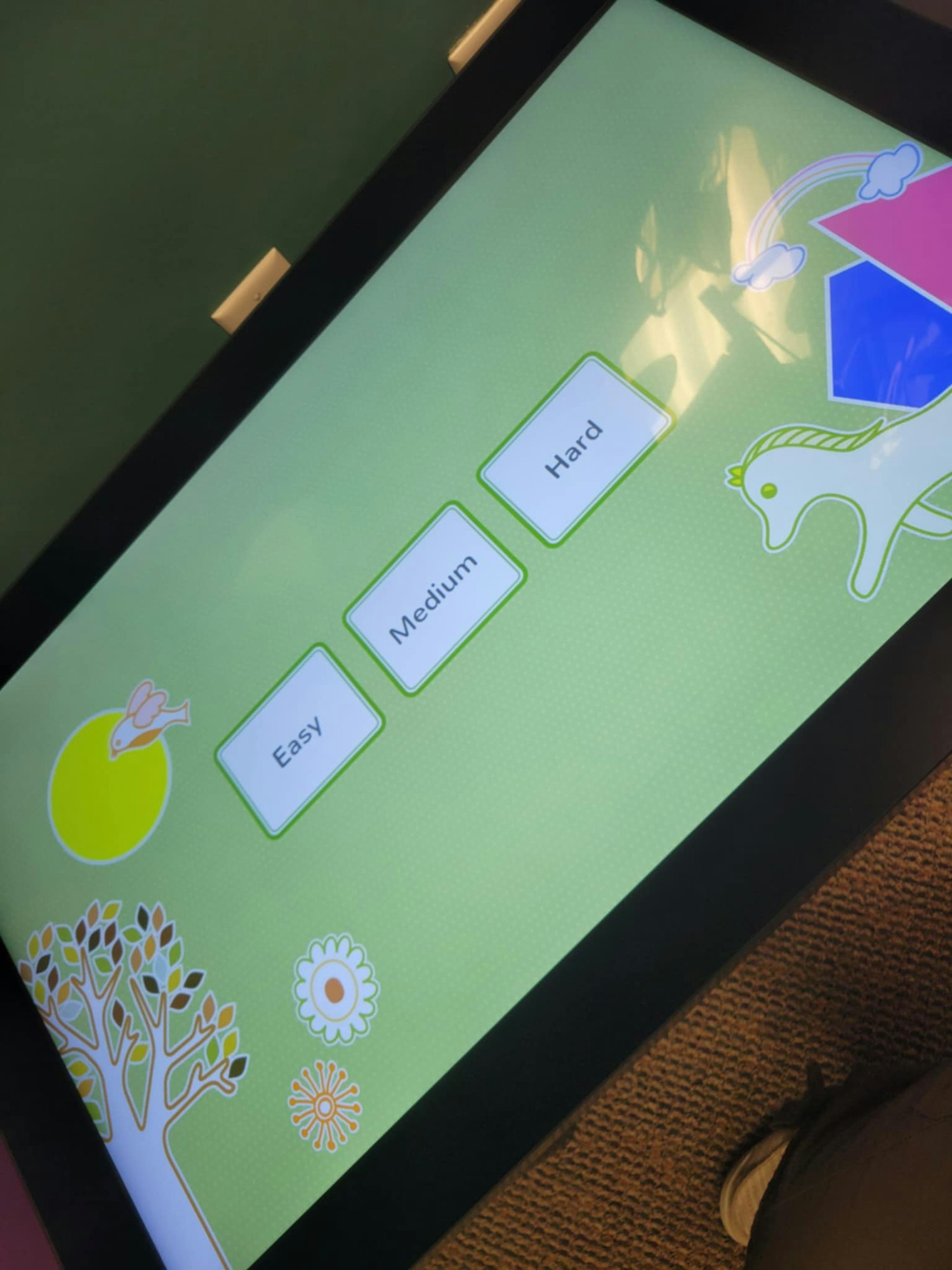A touchscreen displays "Easy," "Medium," "Hard" difficulty options with colorful graphics of a tree, bird, and horse.