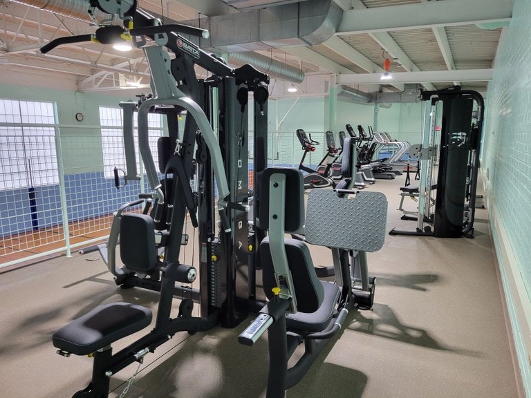 A gym with weight machines, treadmills, and exercise bikes lined up in a well-lit room.