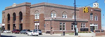A brick building on a street corner with multiple arched windows, cars parked nearby, and a traffic light.