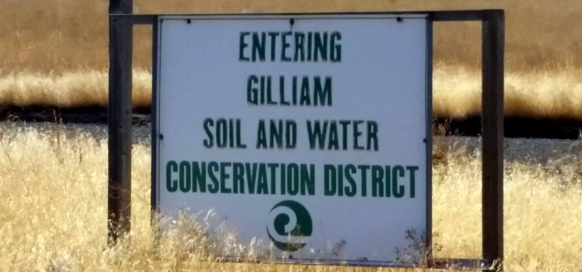 Sign: "Entering Gilliam Soil and Water Conservation District" with a green logo, surrounded by dry grass.