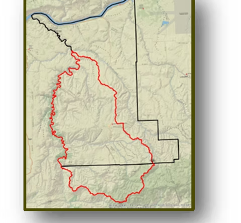 A map with a red outlined area inside a larger black bordered region, featuring a blue river running along the top edge.