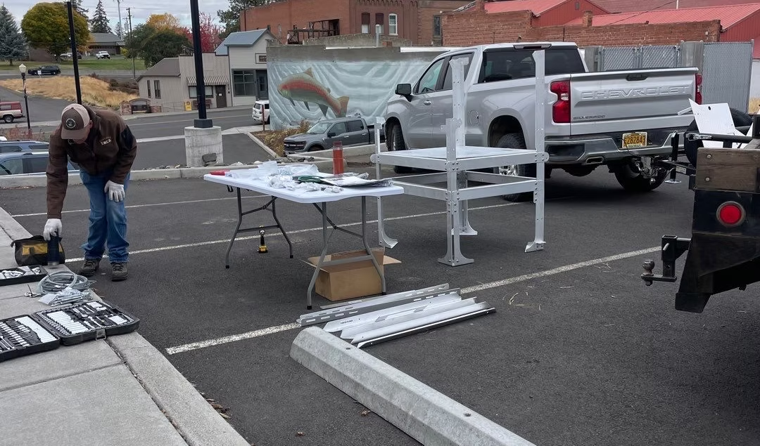 A person assembling equipment in a parking lot with tools, a table, and a truck nearby.
