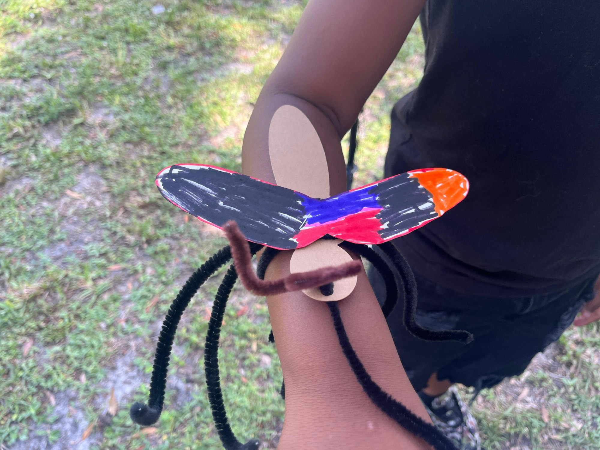 A handmade paper butterfly with a pipe cleaner body on a child's arm.
