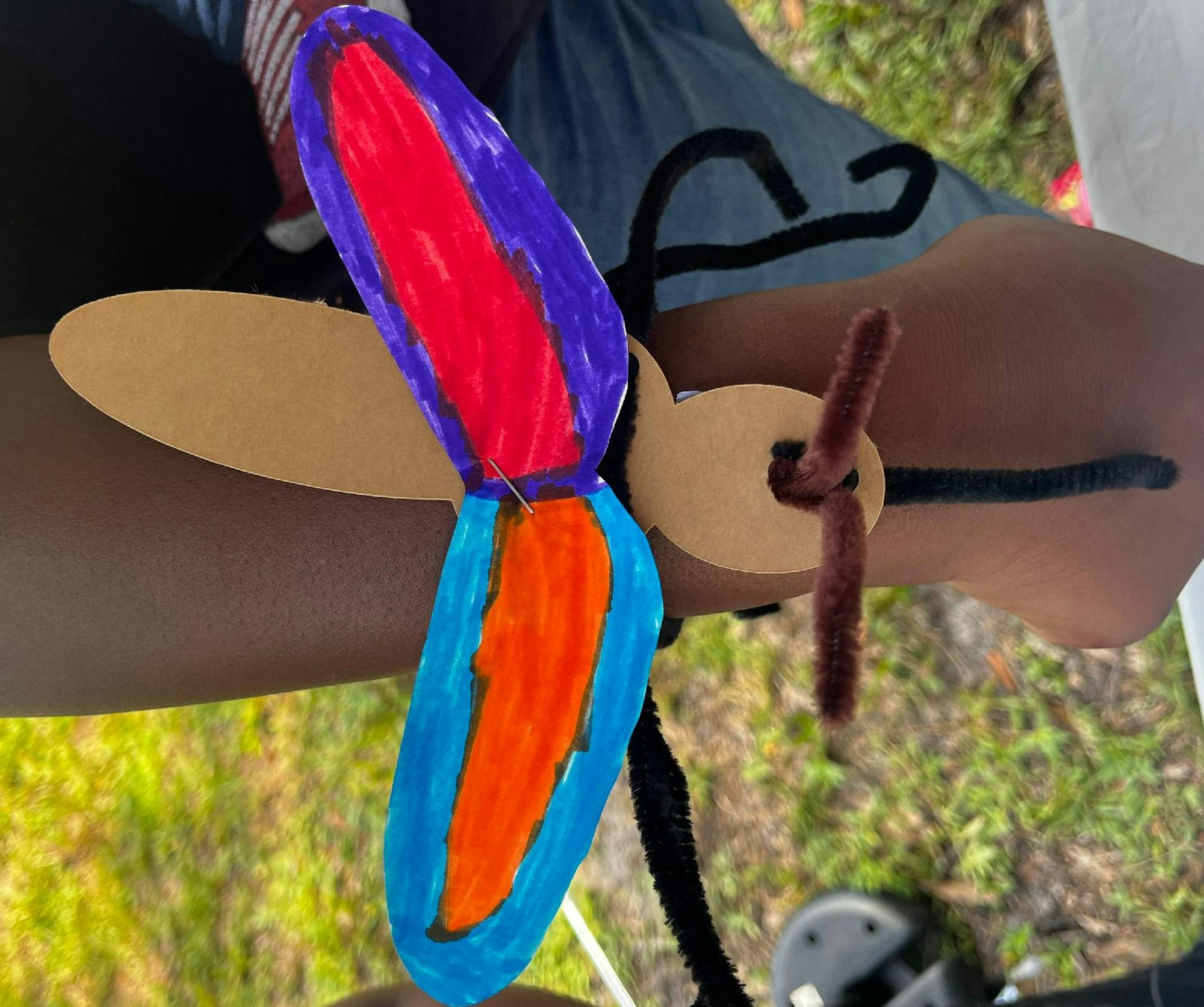 A child's arm with a handmade paper and pipe cleaner butterfly bracelet.