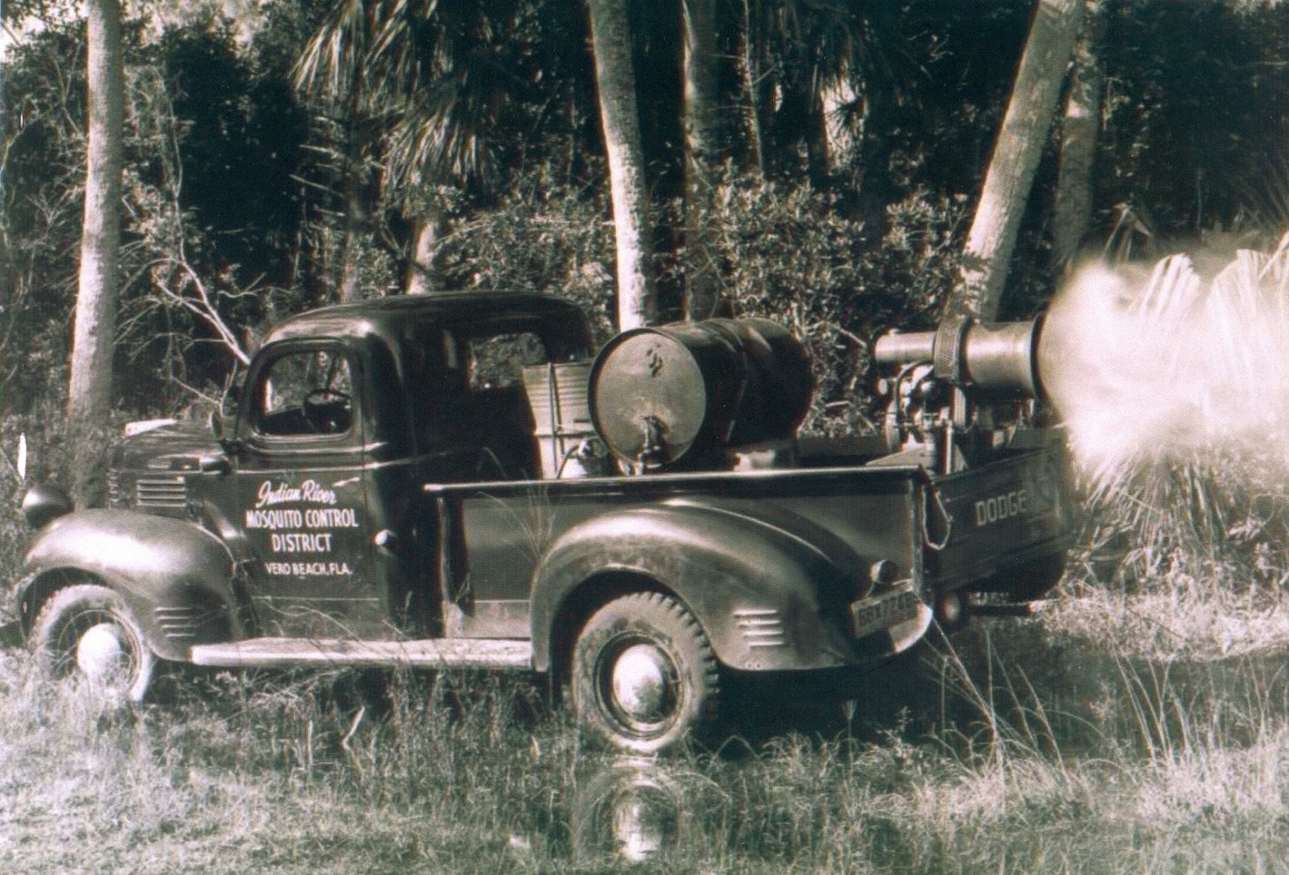 Vintage mosquito control truck emitting a fog of insecticide.