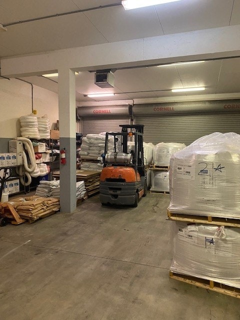 A warehouse with stacked bags, a forklift, and pallets on the floor.