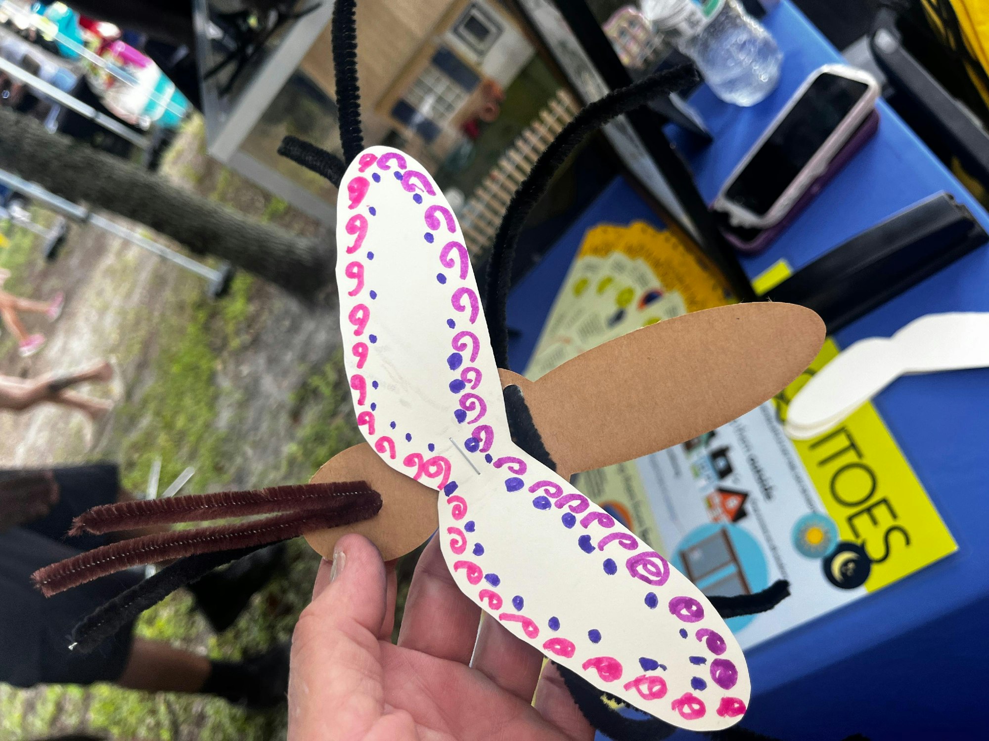 Handmade craft butterfly with decorated paper wings and pipe cleaner antennae held by a person.