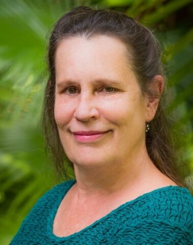 A smiling woman with a green, leafy background.