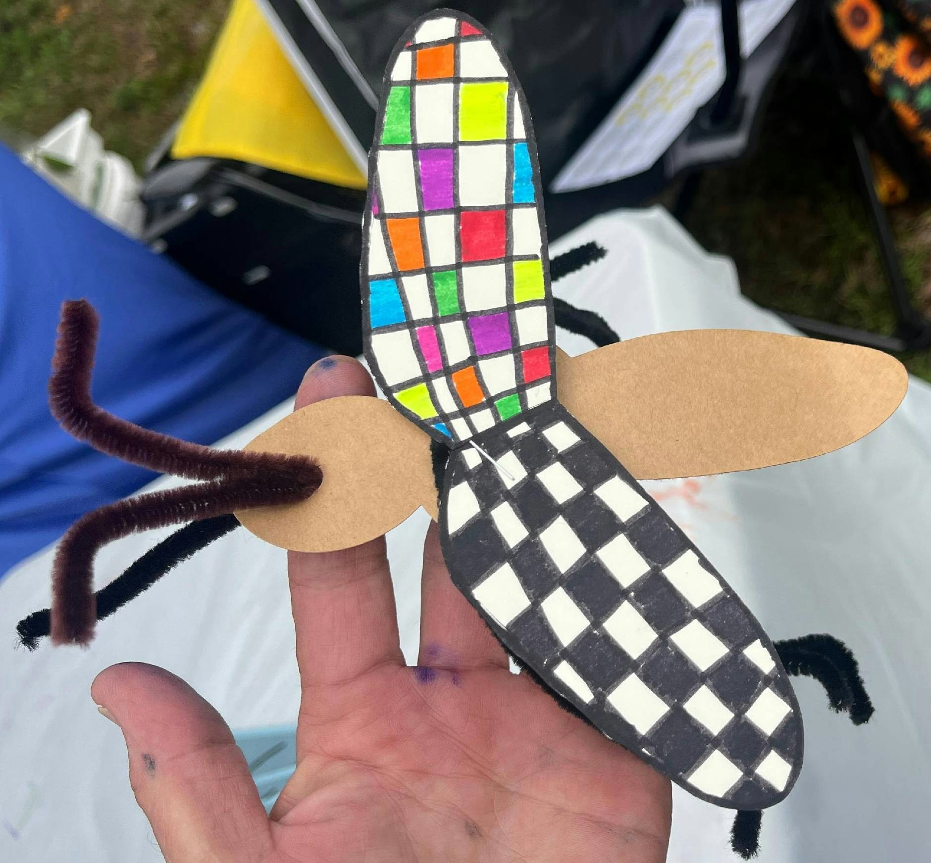 A hand holding a colorful, handmade cardboard bee craft.