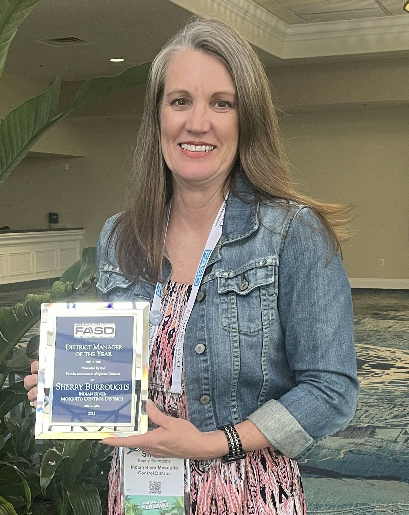 A woman smiling, holding an award for "District Manager of the Year".