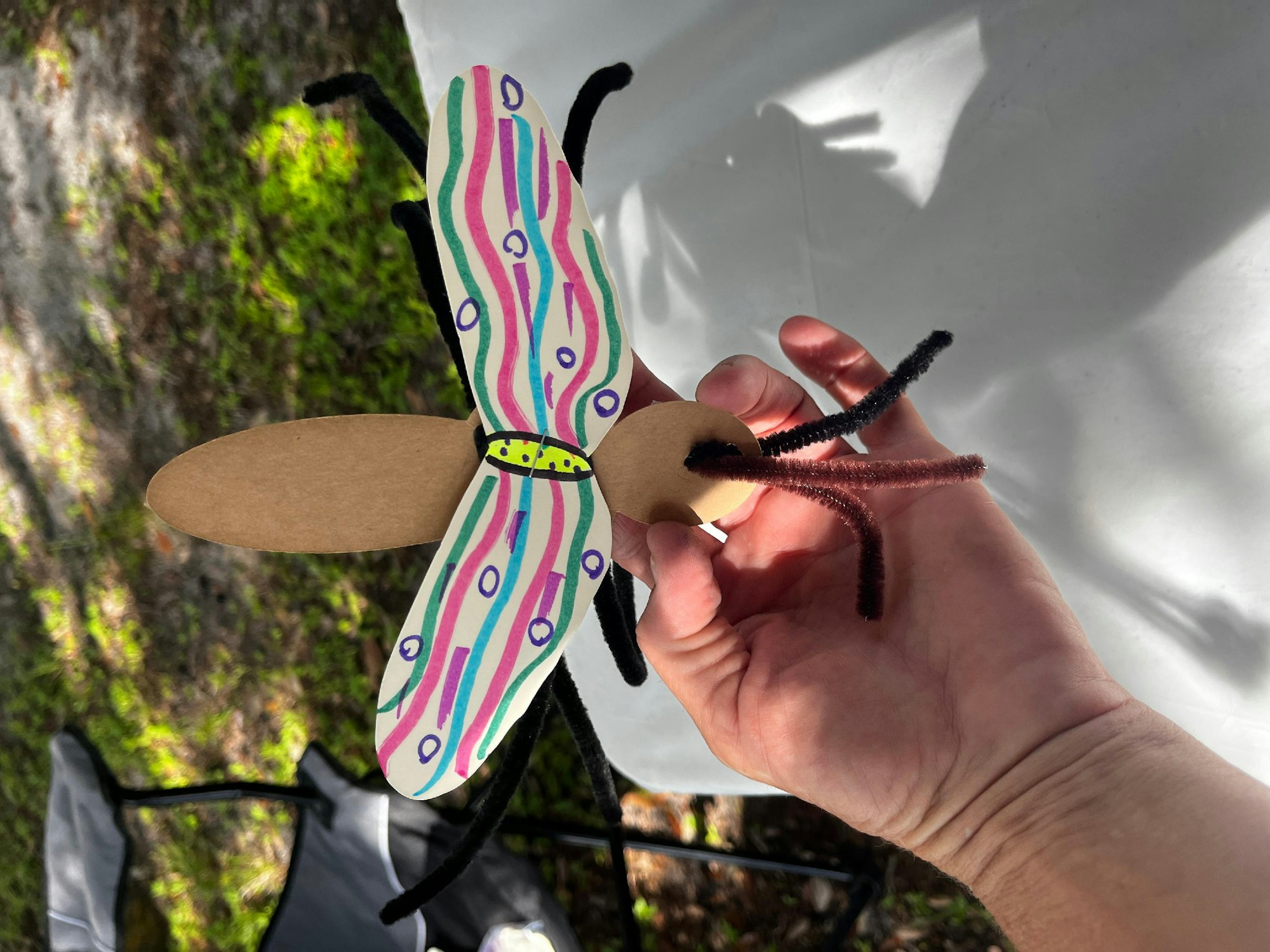 A hand holding a colorful handmade paper butterfly with pipe cleaner antennae.