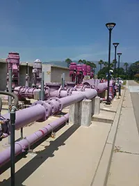 The image shows a series of purple pipes and valves, likely part of a water treatment or distribution system, under clear skies.