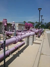 The image shows a series of purple pipes and valves, likely part of a water treatment or distribution system, under clear skies.